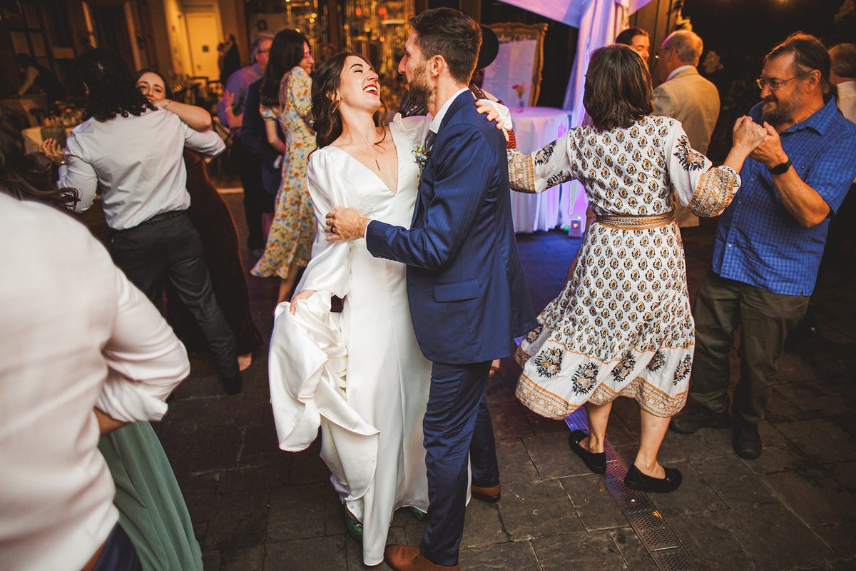 Andrea laughing with her head back as Patrick holds her close on the dance floor, her skirt gathered in one hand and couples spinning on both sides