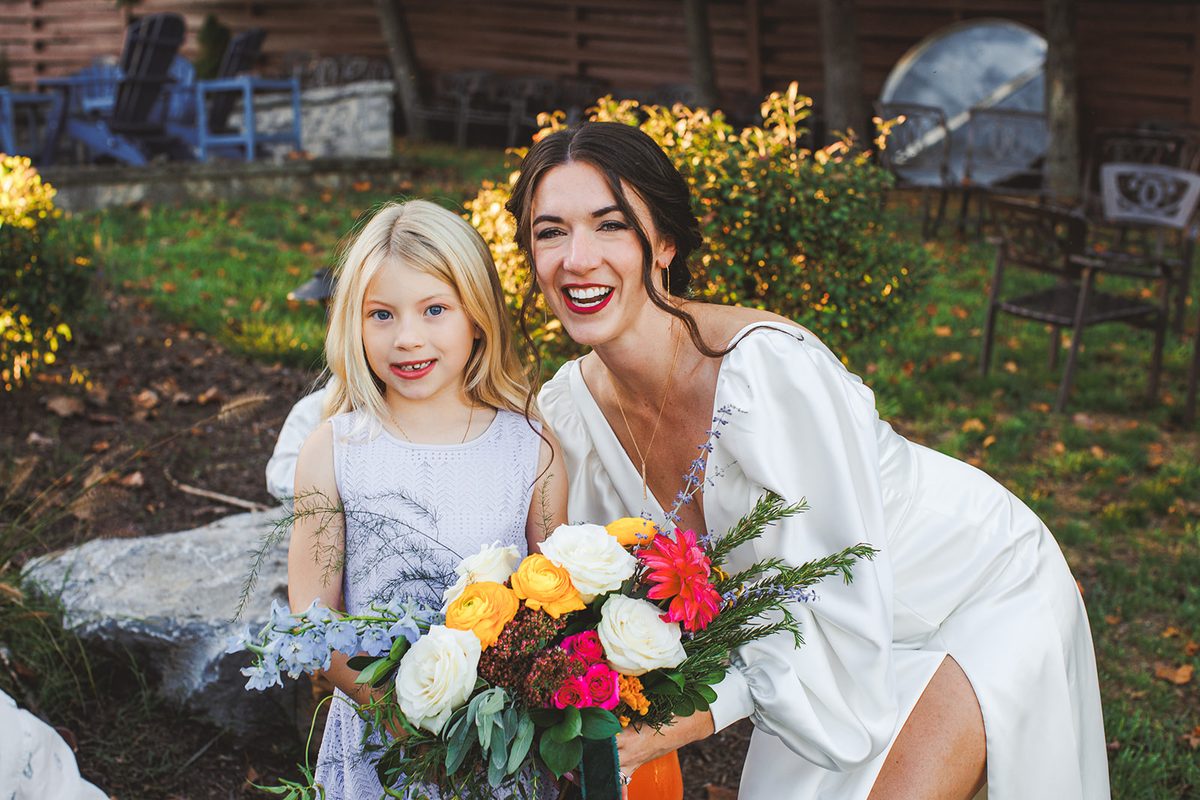 Andrea kneeling with her bouquet beside the flower girl in lavender, both smiling
