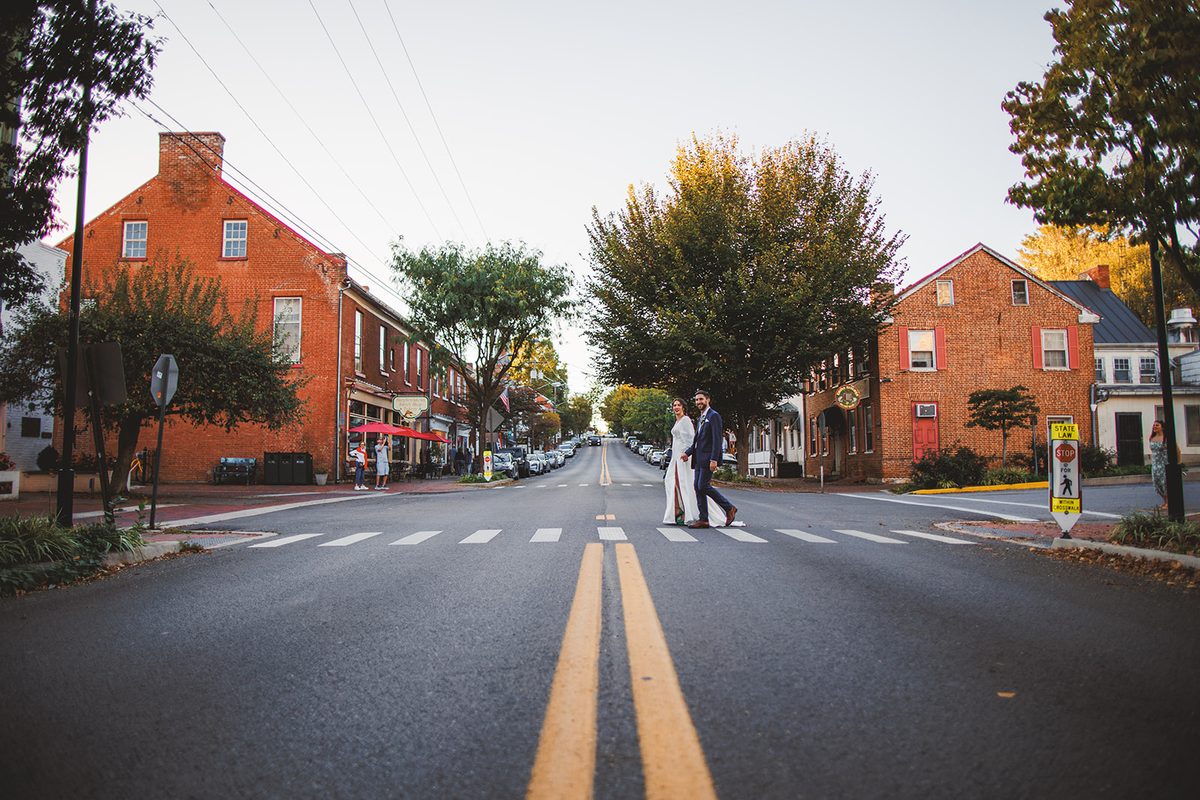 Andrea and Patrick crossing German Street in downtown Shepherdstown, brick buildings and autumn trees lining the empty road