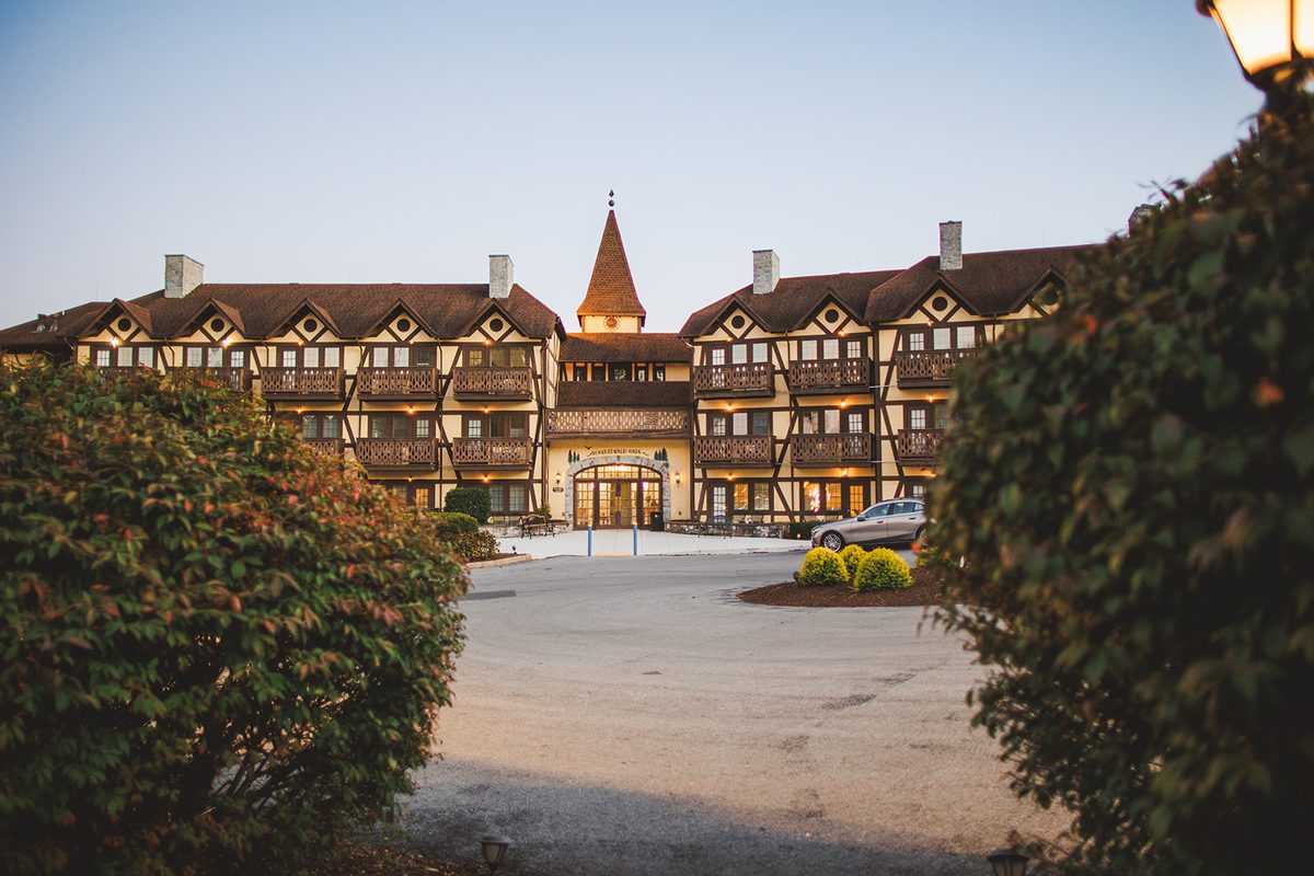 The main half-timbered building of the Bavarian Inn at dusk, its turret and balconies lit warm against a pale blue sky