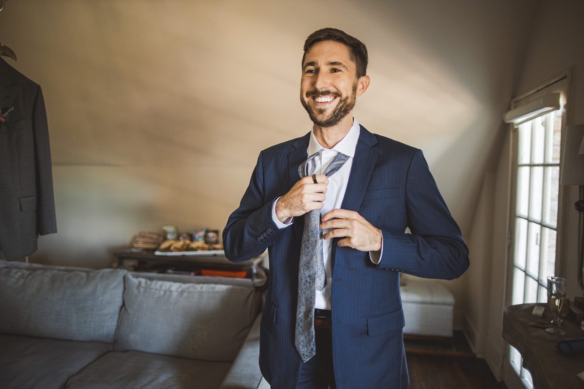 Patrick smiling as he adjusts his tie in the chalet loft before the ceremony