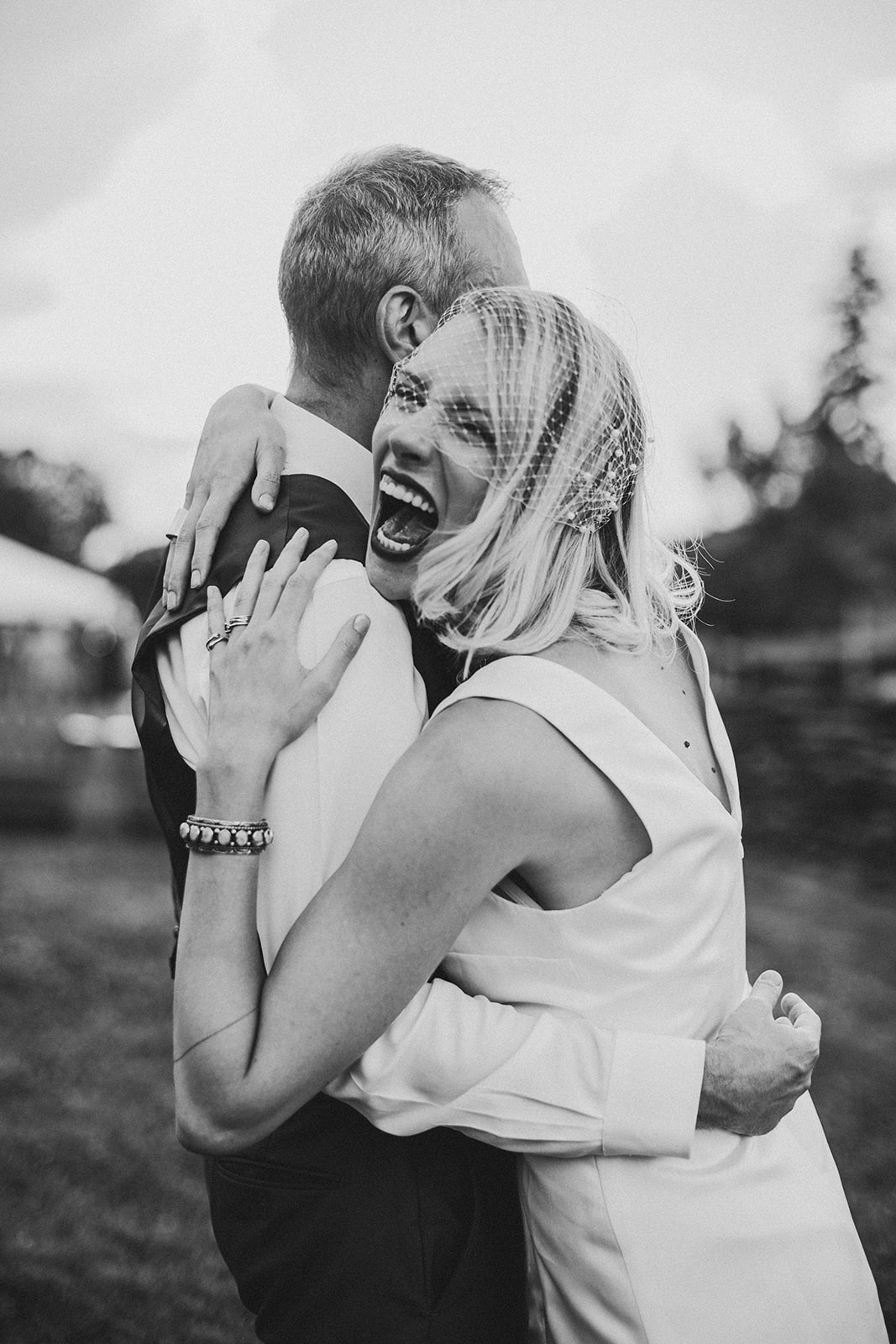 Black and white frame of Annie laughing over Thomas's shoulder mid-embrace, her birdcage veil pushed up