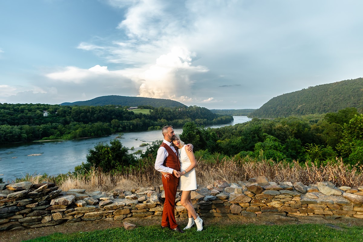 Annie leaning into Thomas at the overlook wall as a huge storm cloud glows over the Potomac water gap behind them