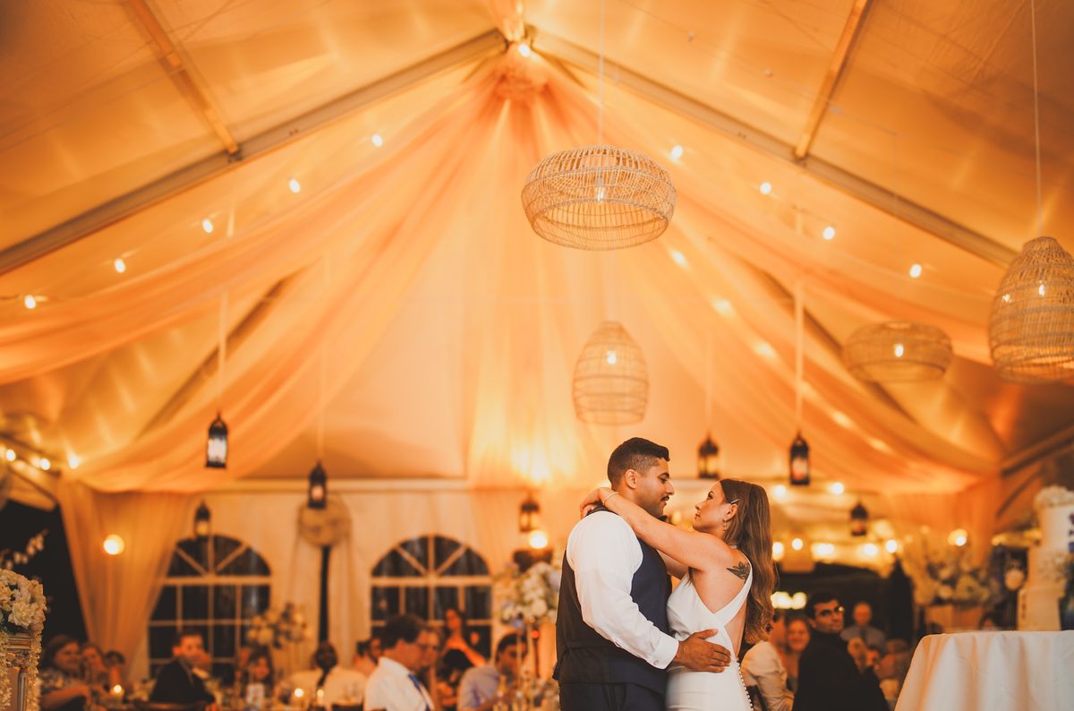 Wide view of the draped amber tent with woven lanterns glowing overhead as Bailey and Youssef dance at its center