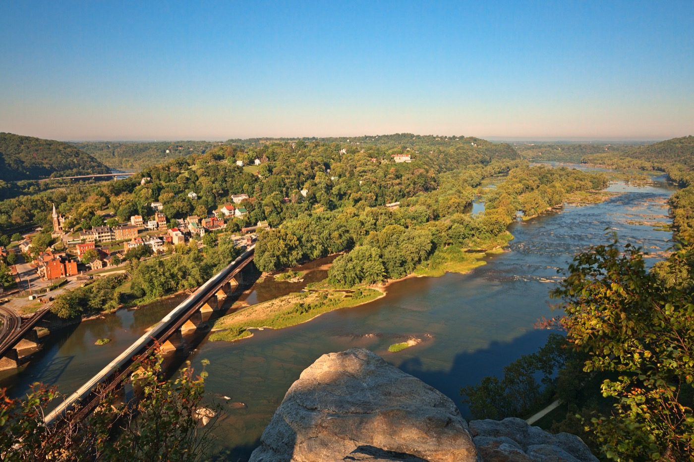 Harpers Ferry from the heights above, the town on the point where two rivers meet, the railroad bridge crossing below and wooded ridges running into the distance