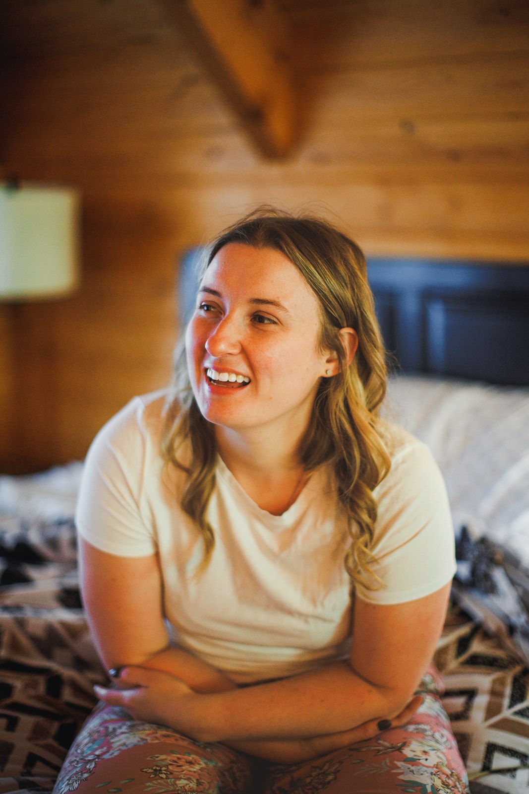 Michaela sitting cross legged on the bed in the cabin before the ceremony, laughing at something off camera