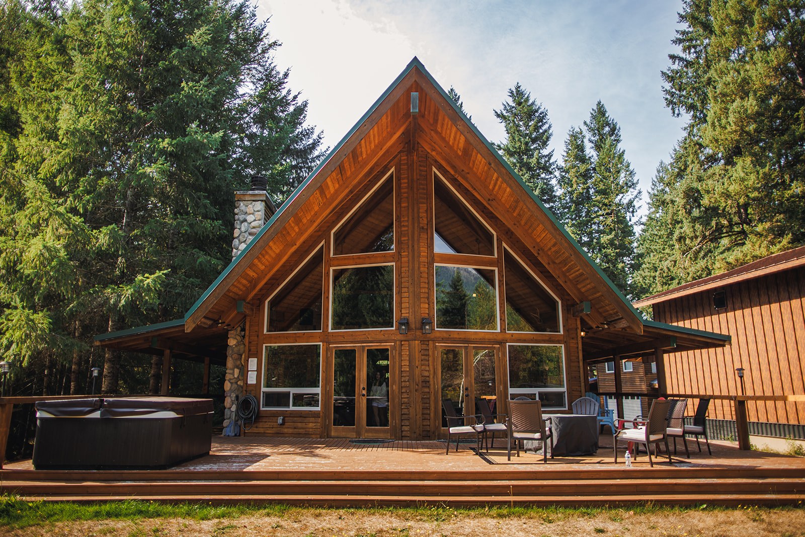 The A frame cabin with a green metal roof and a tall glass gable, surrounded by evergreens