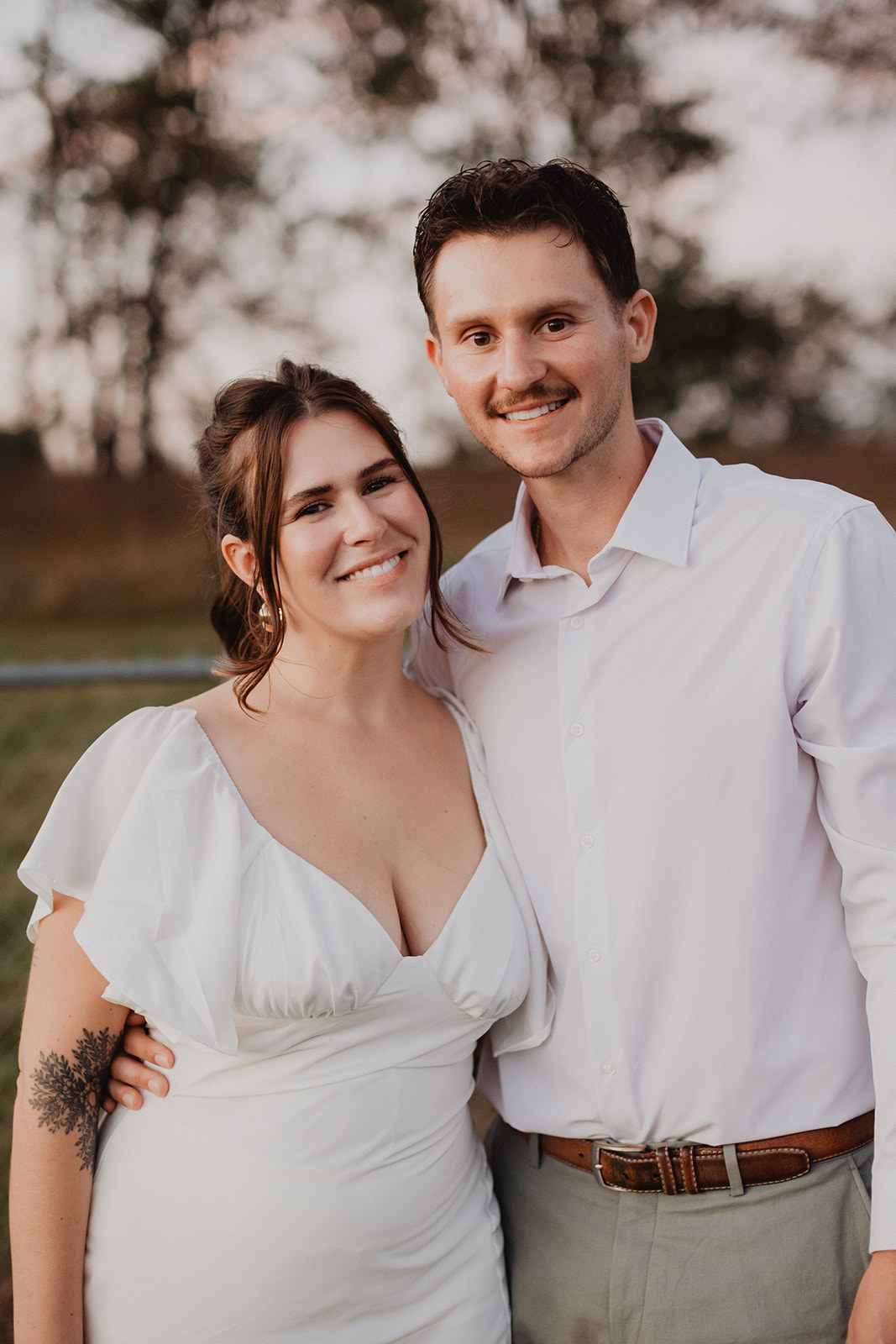 Michaela and AJ standing together on the lawn at dusk, bare trees and pale sky behind them