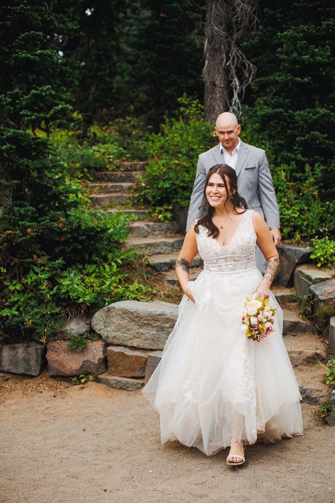 Michaela coming down a set of stone steps toward the ceremony with her father behind her, both of them smiling