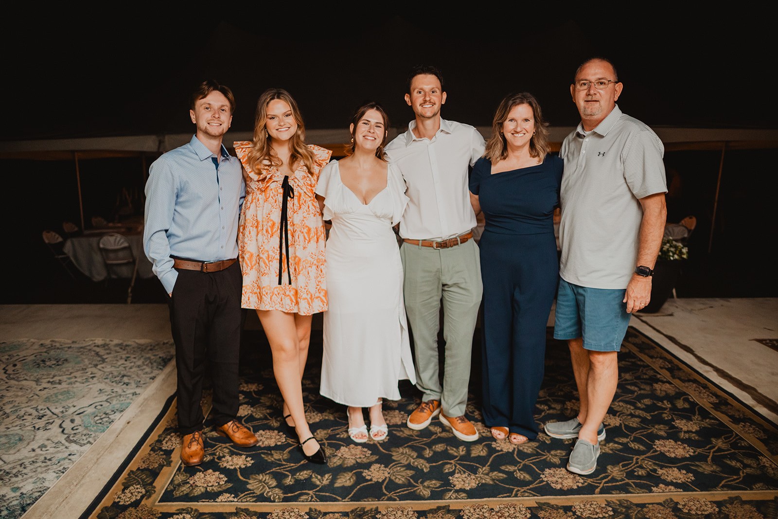 Guests gathered close together on the dark lawn at the end of the night, lit warm against the glow of the tent behind them
