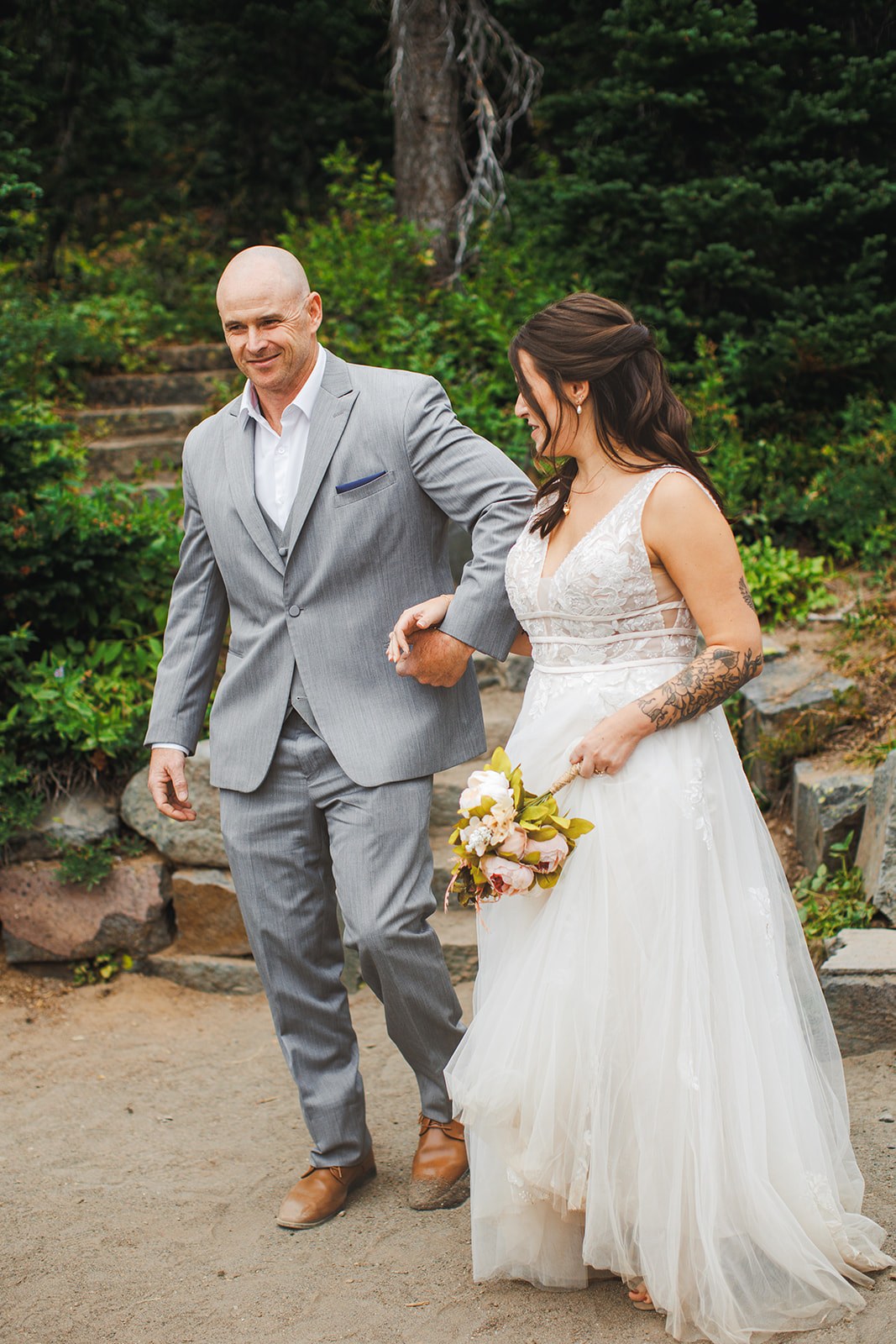 Michaela's father walking her the last of the gravel path in his grey suit, her bouquet in her free hand
