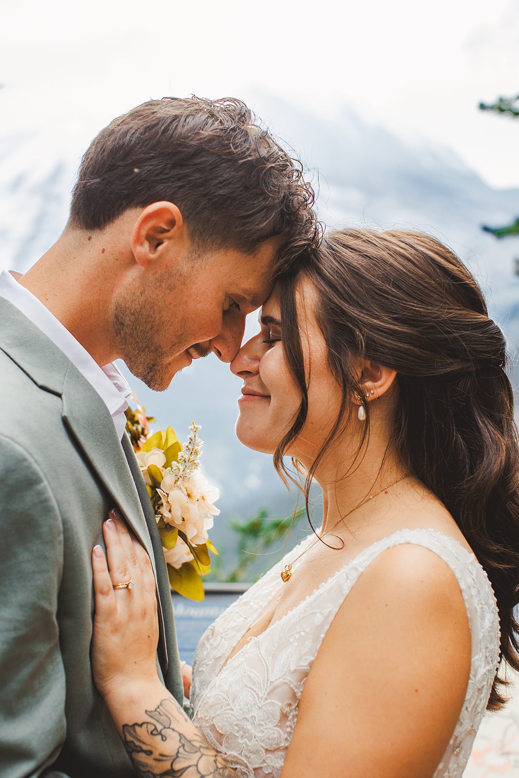 Michaela and AJ resting forehead to forehead on the trail, her hand flat on his chest, the hazy mountain soft behind them