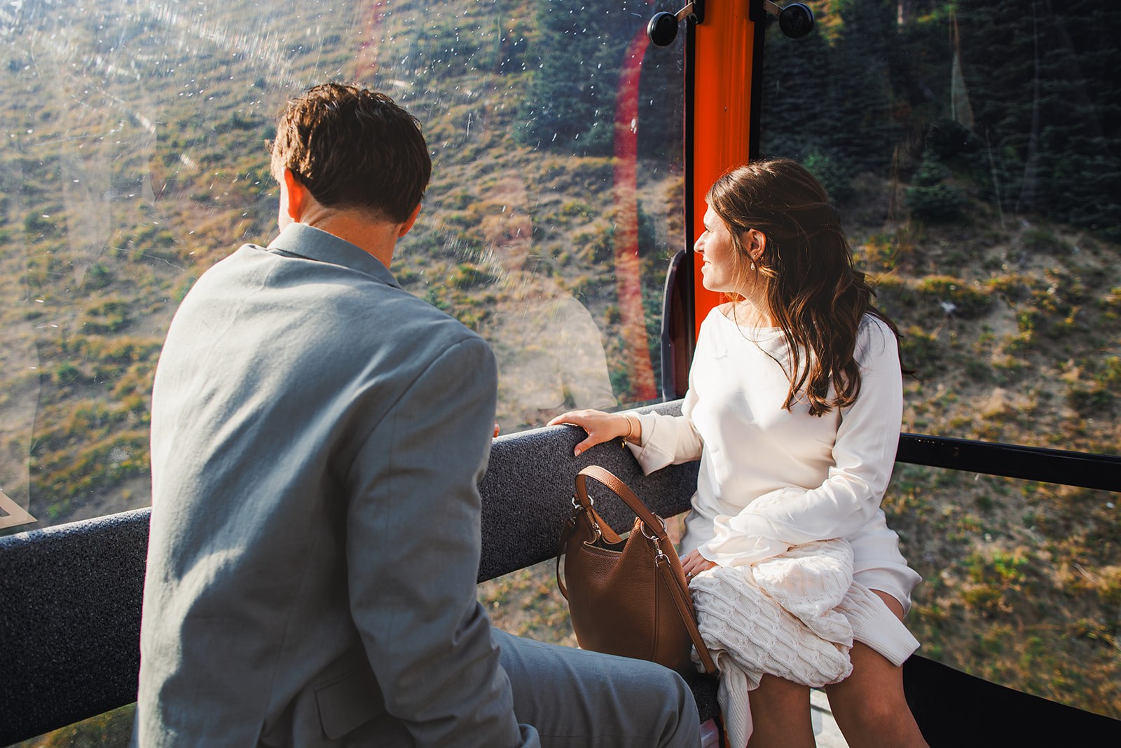 Michaela and AJ sitting across from each other in the gondola looking out at the forested slope sliding past below them