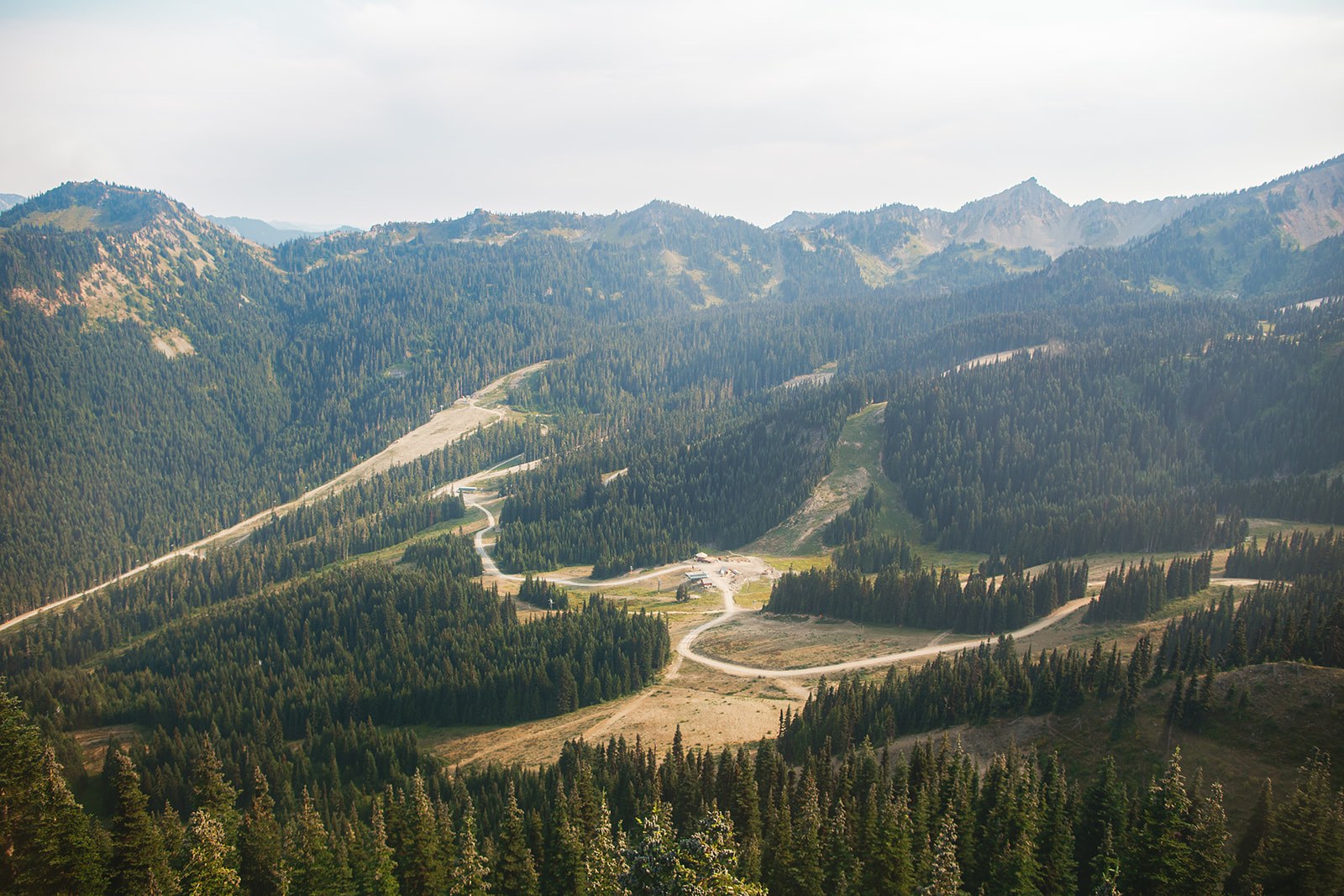The view down from the gondola: a long green valley of firs and ski runs with bare rocky ridgelines stacked along the skyline