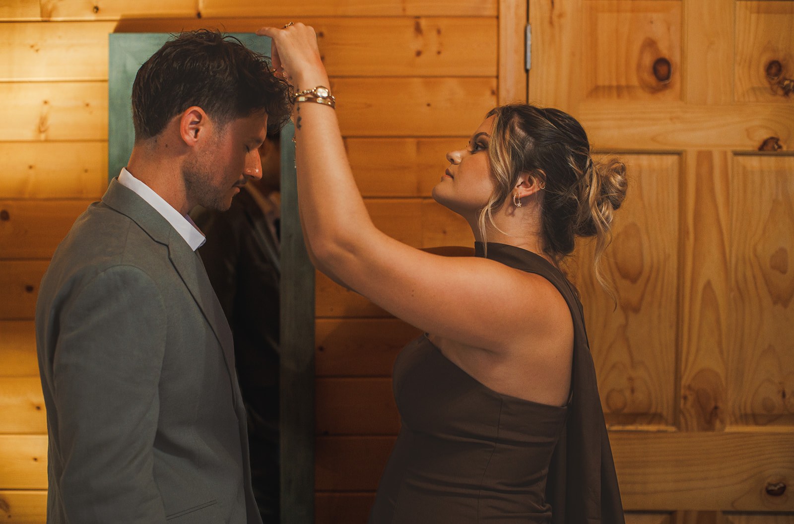 A friend reaching up to straighten AJ's collar in the cabin doorway, his sage linen jacket already on