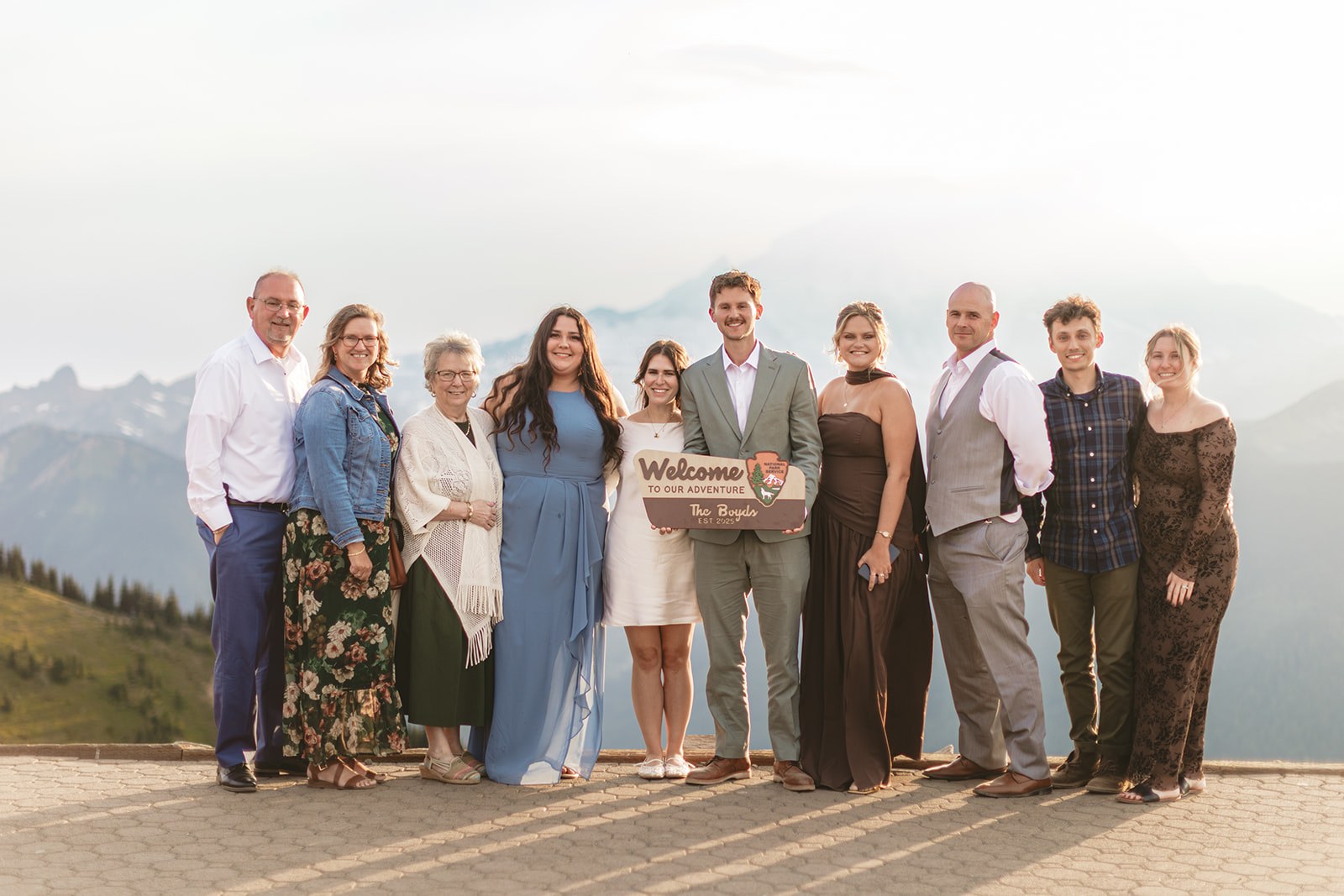 All ten of them standing shoulder to shoulder on the summit deck at sunset holding the wooden Boyds sign, hazy blue ridges falling away behind