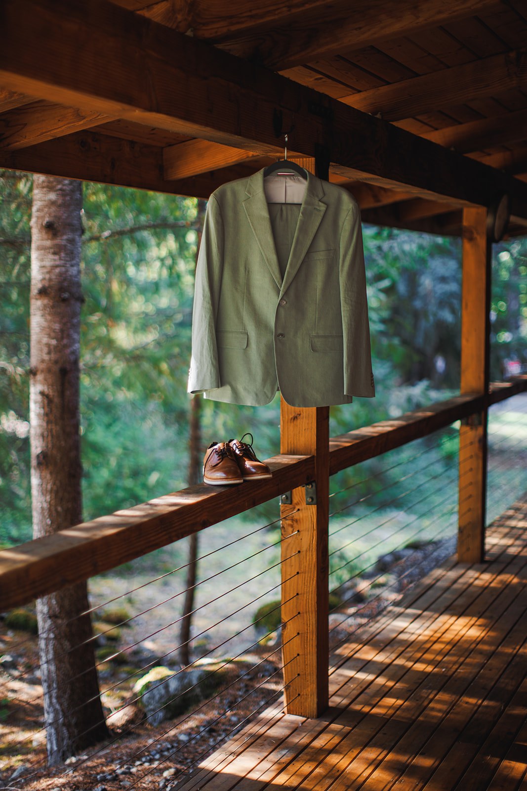 AJ's sage linen jacket hanging from the cabin porch beam with his brown leather shoes set on the rail below it