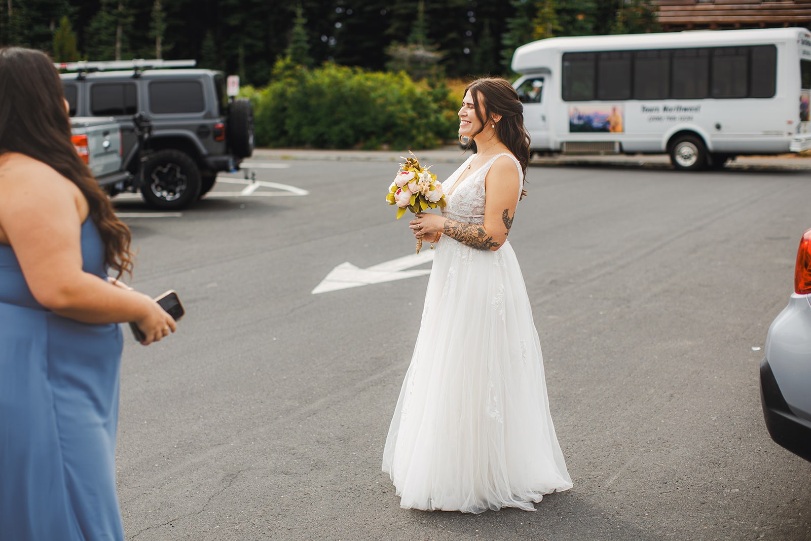 Michaela standing in the Sunrise parking lot in her wedding dress holding her bouquet, a tour bus and parked cars behind her
