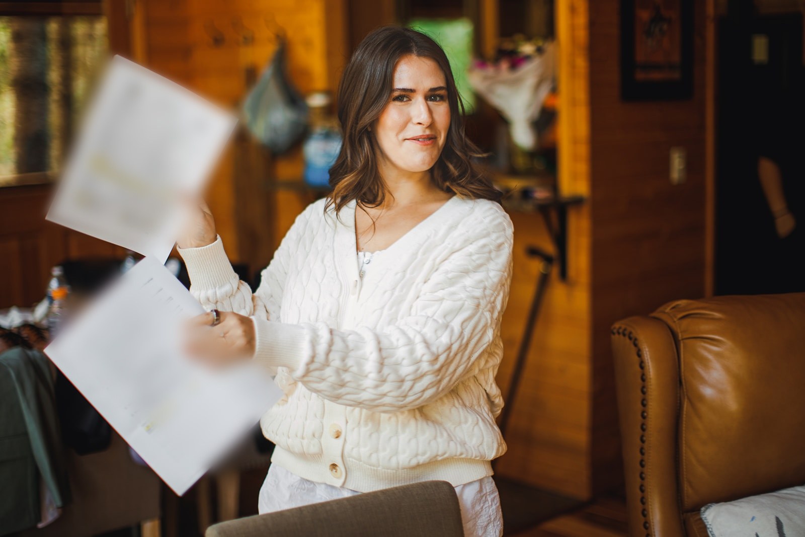 Michaela in a cream cable knit sweater holding up two pages of her Mount Rainier National Park special use permit in the cabin, half smiling at the camera
