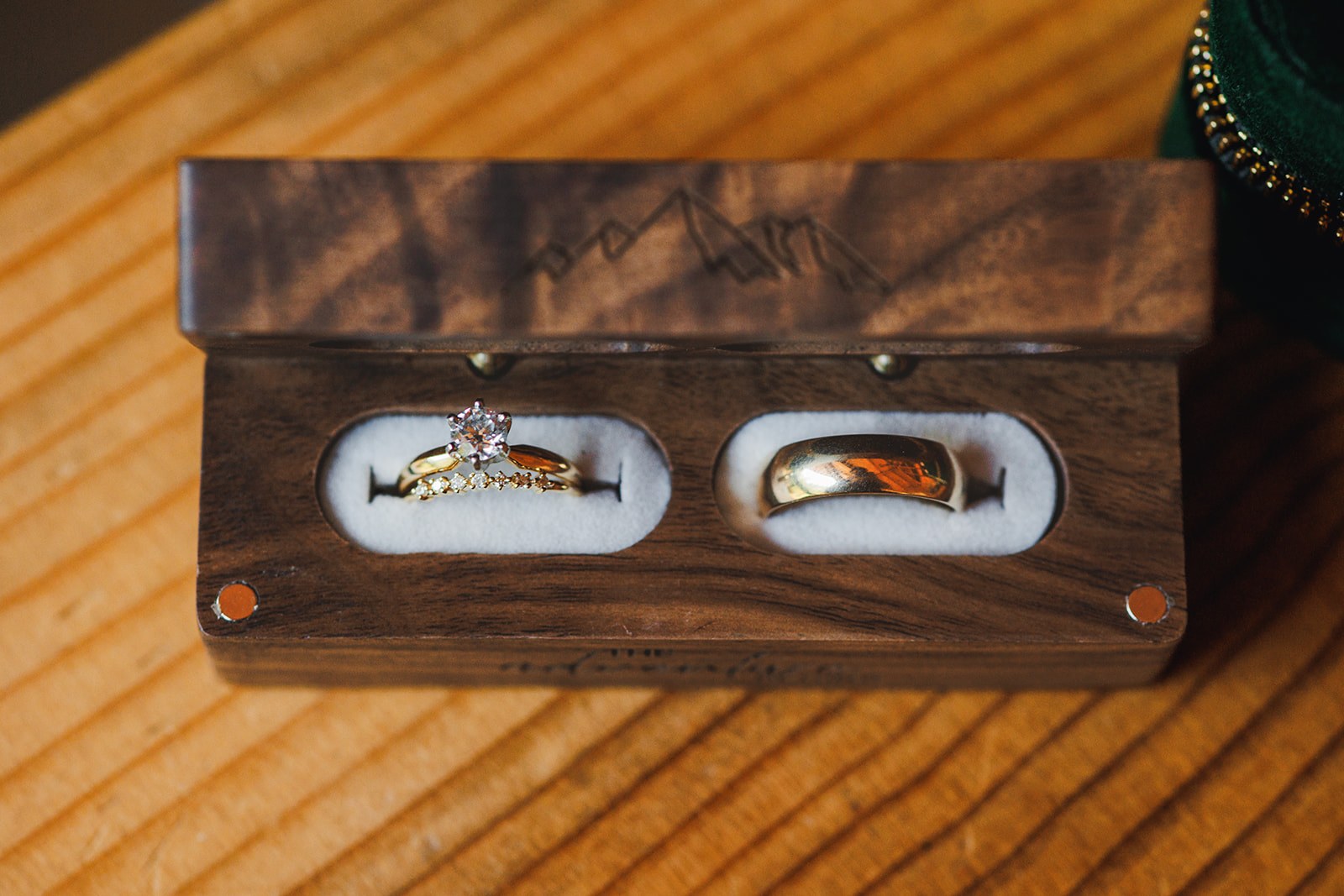 Two wedding bands and an engagement ring set into a walnut ring box with a mountain range engraved on the lid