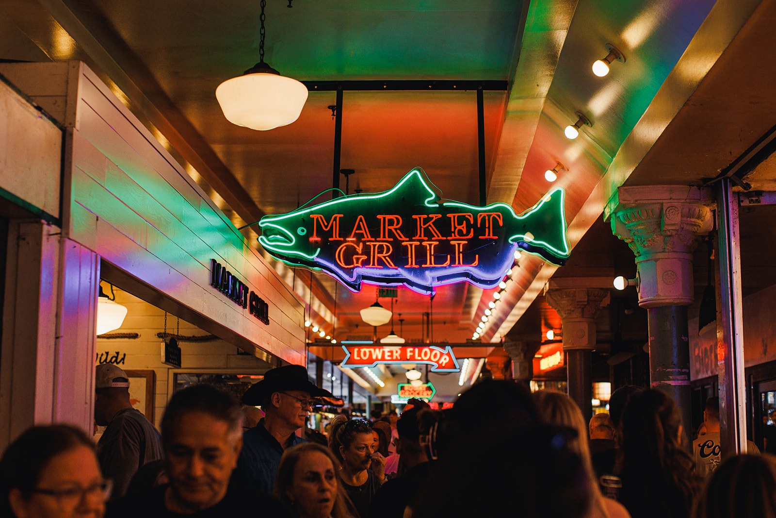 The green and red Market Grill neon fish sign glowing in the crowded lower arcade of Pike Place Market