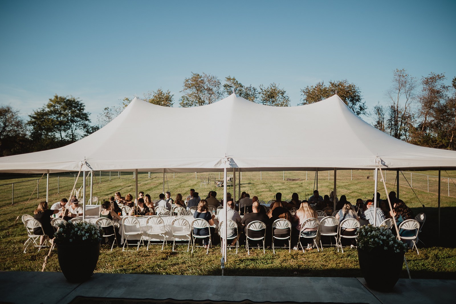The tent from across the field in low gold light, guests seated the full length of both tables