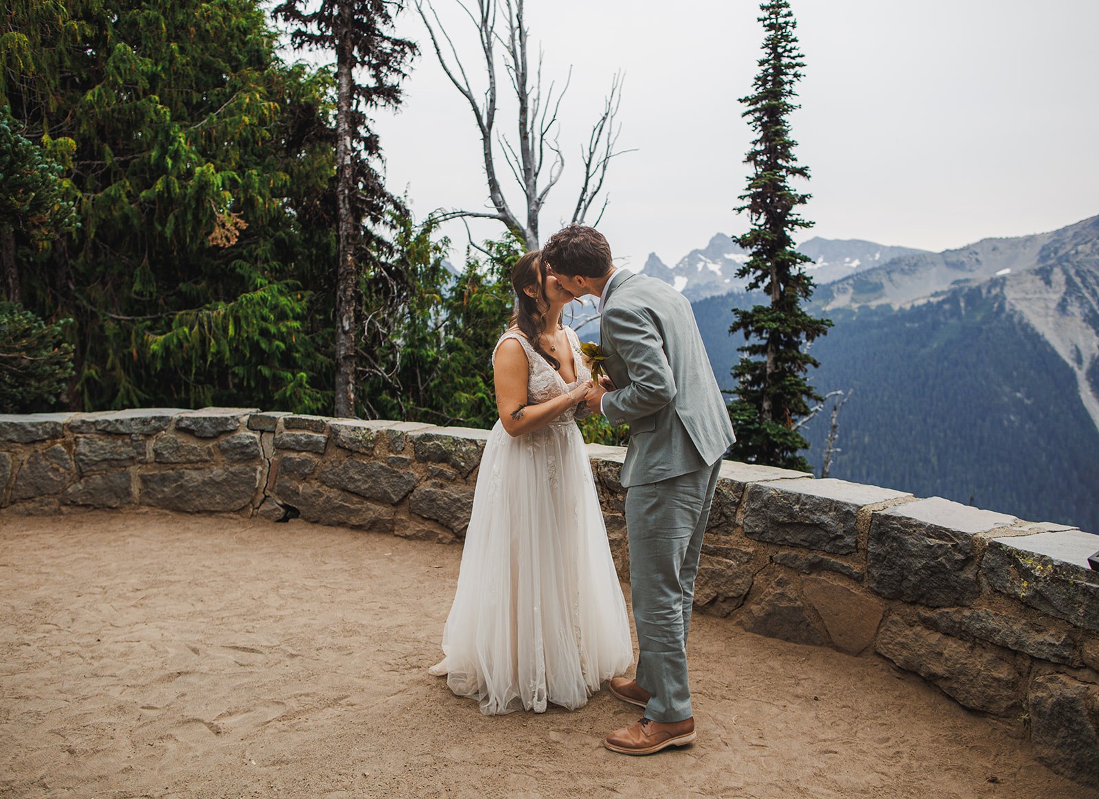 Michaela and AJ alone on the empty stone terrace at Emmons Vista, foreheads together, the curved overlook wall and the ridges of Mount Rainier behind them