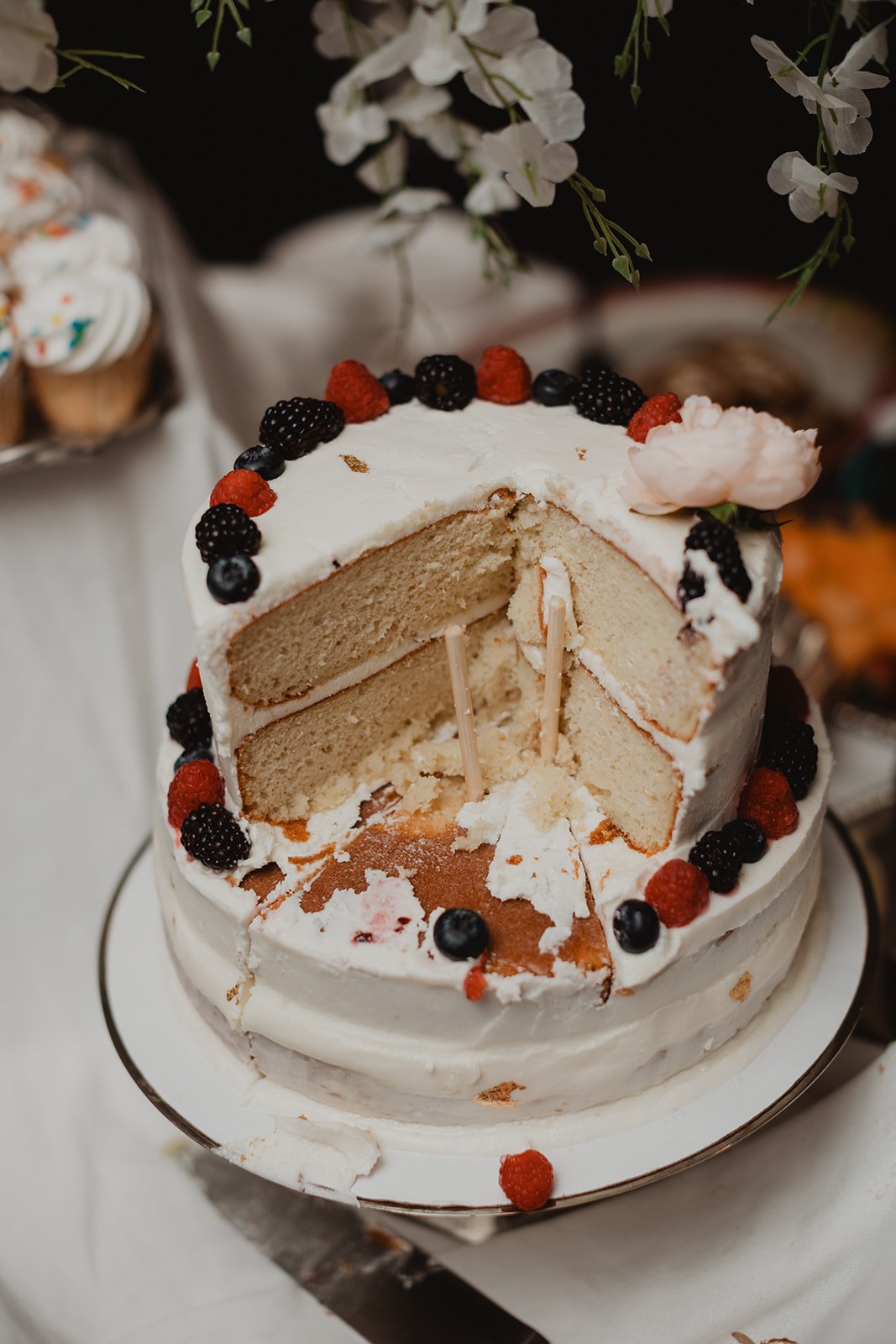 The same cake after cutting, one wedge gone and the pale layers showing, berries still around the rim