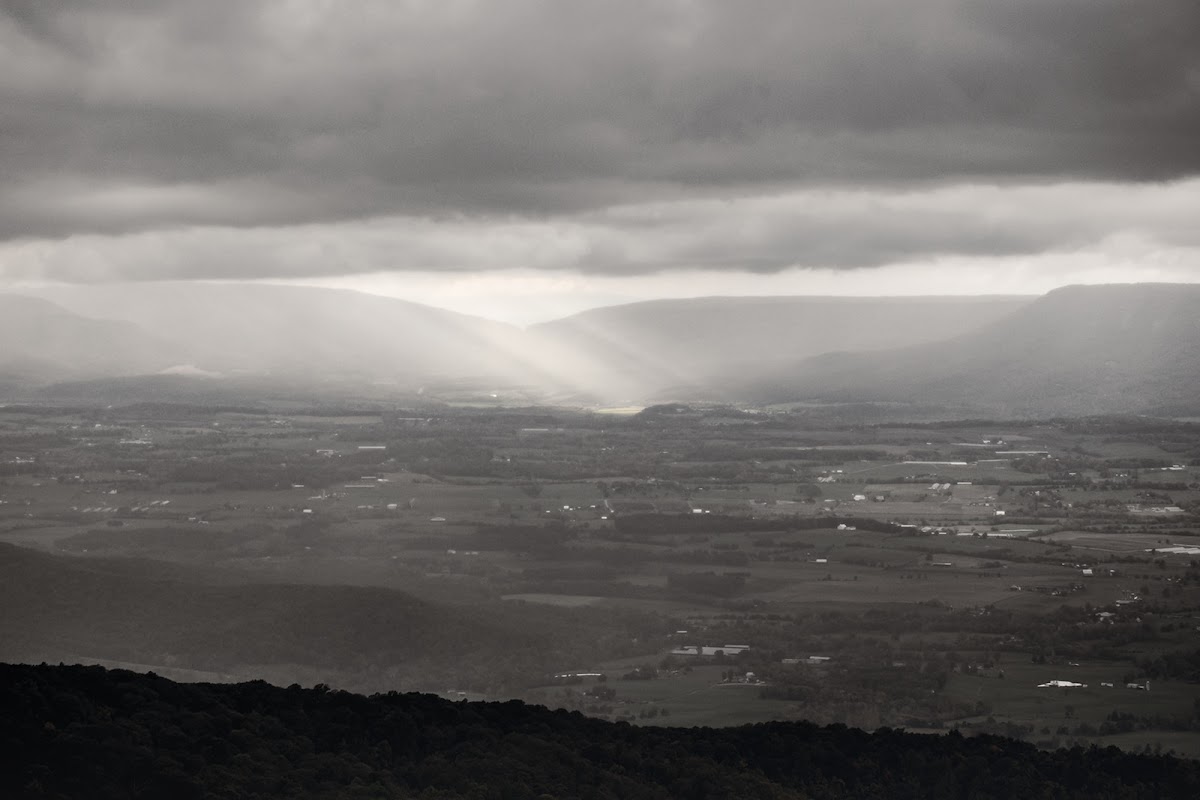 Sunbeams breaking through storm clouds and raking across the Shenandoah Valley floor far below the overlook