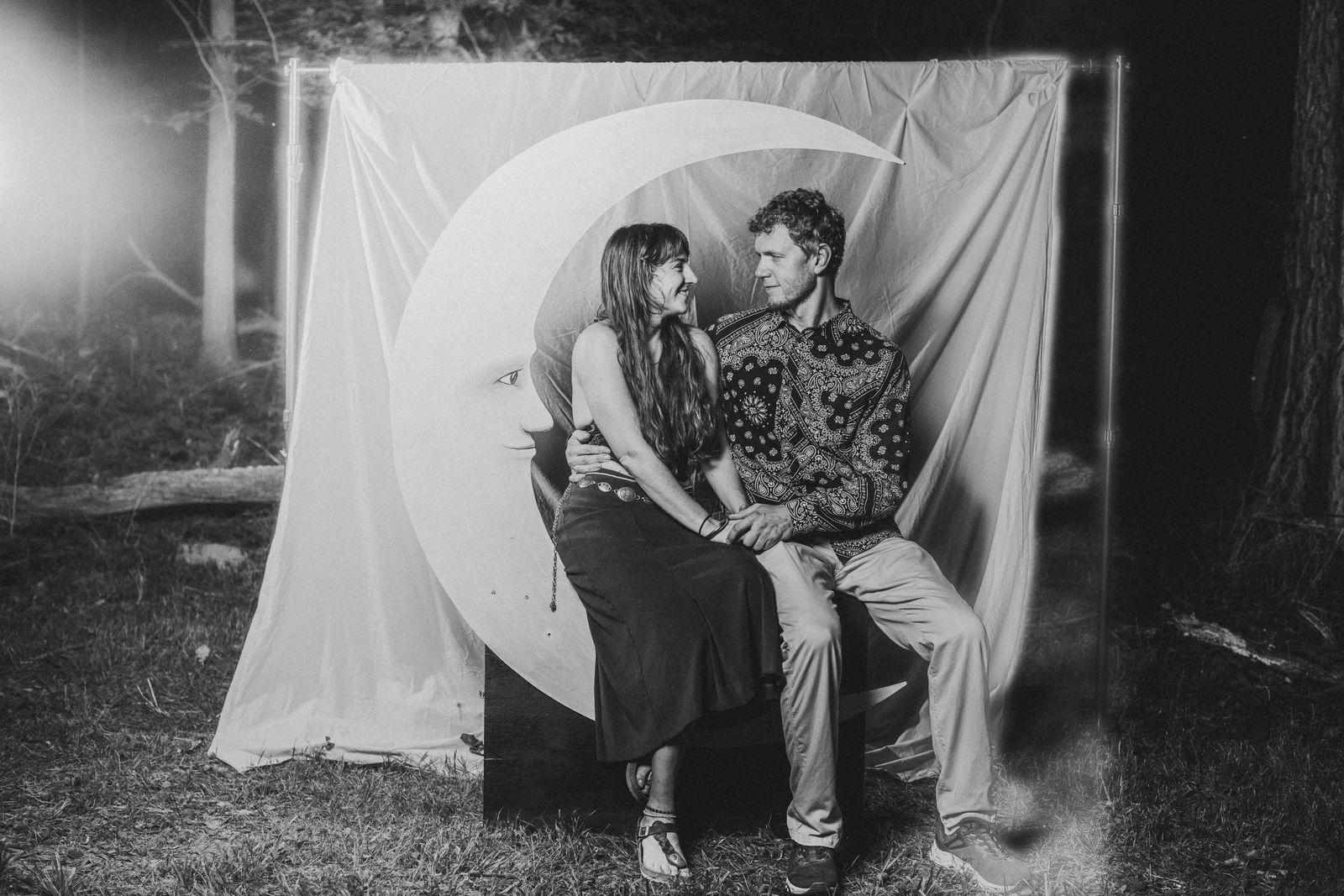 A couple seated together on the crescent moon looking at each other, in black and white