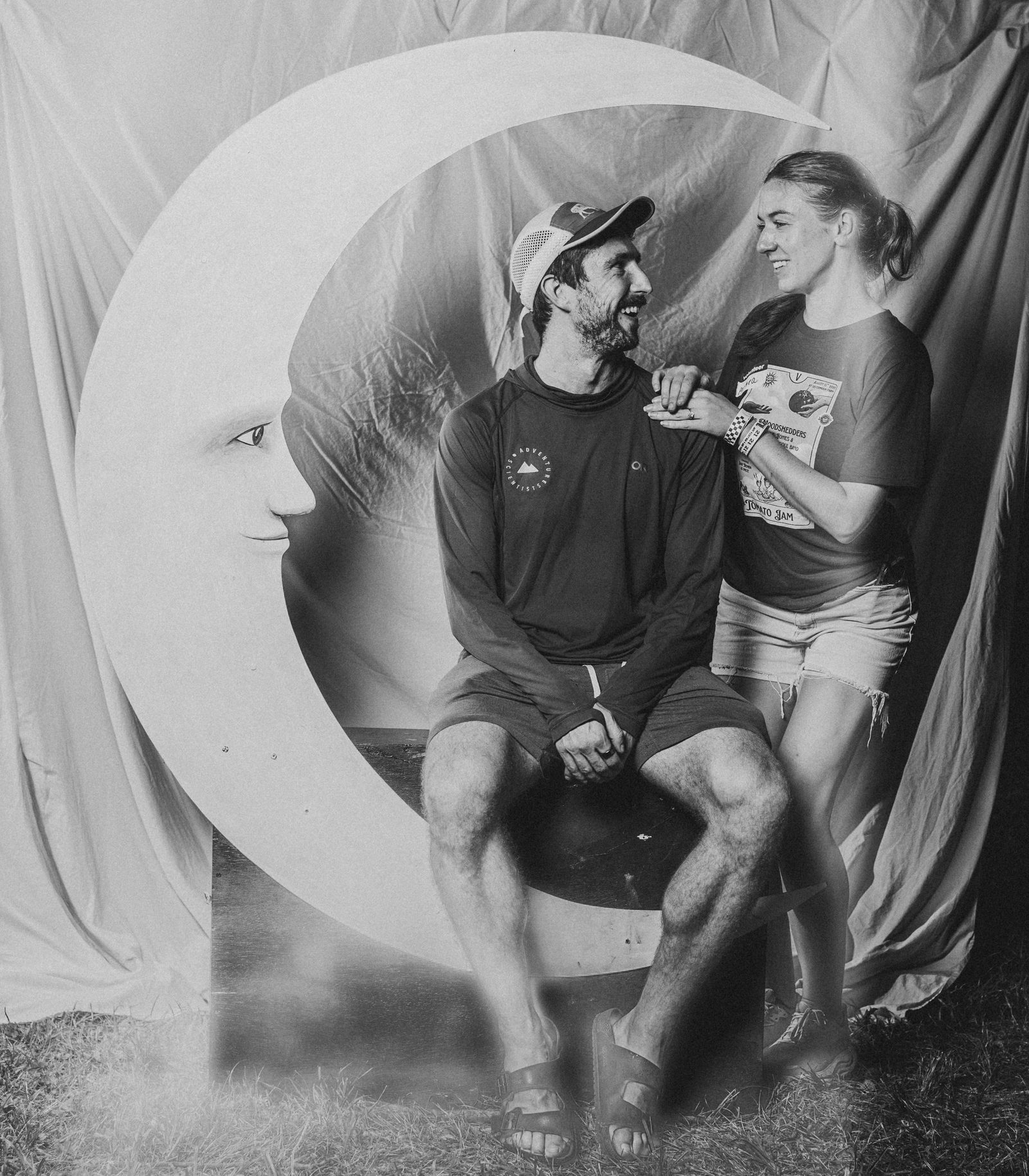 A couple laughing together on the crescent moon at the Moon Booth, in black and white