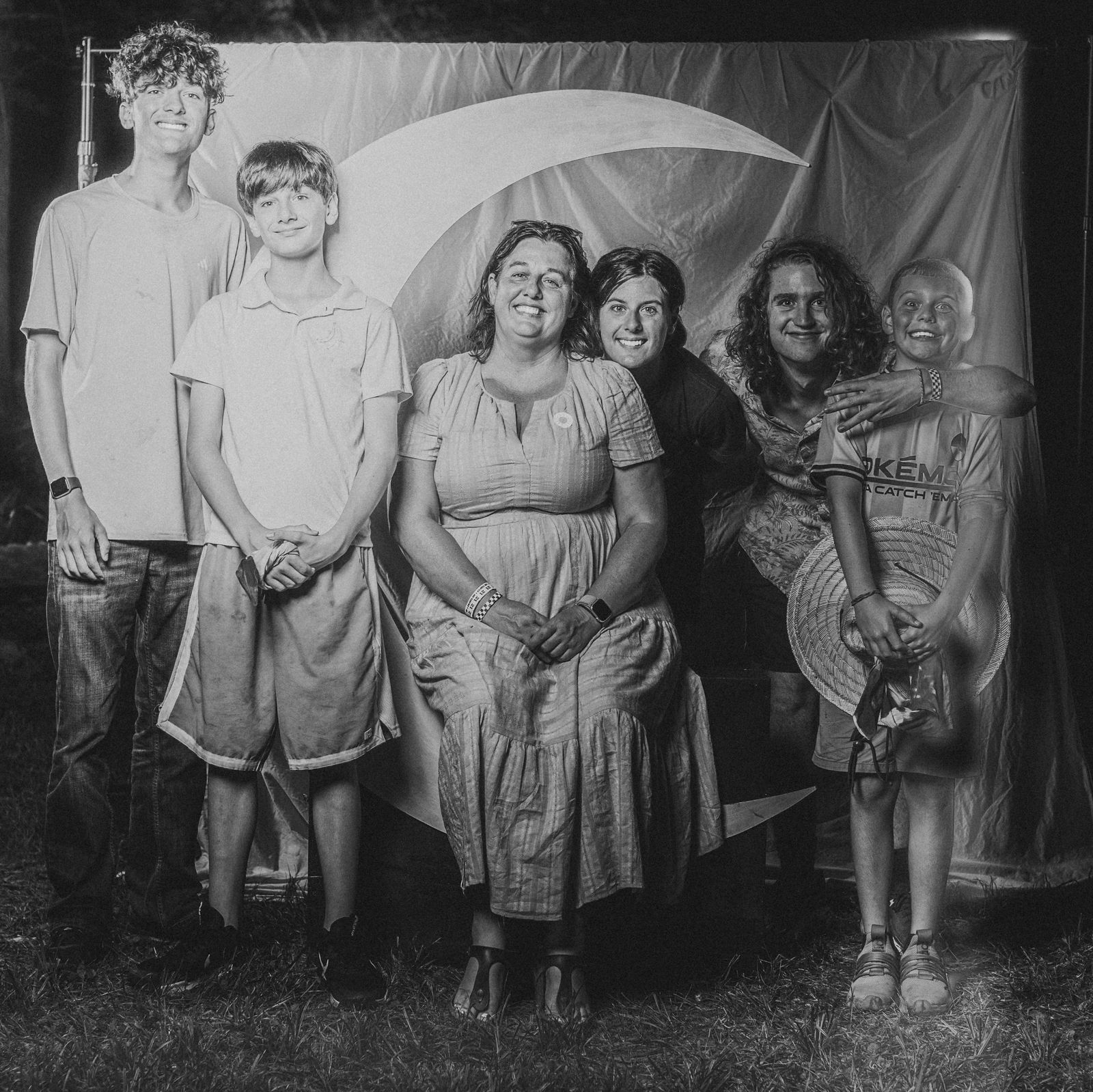 A family of six gathered around the crescent moon at the Moon Booth, in black and white