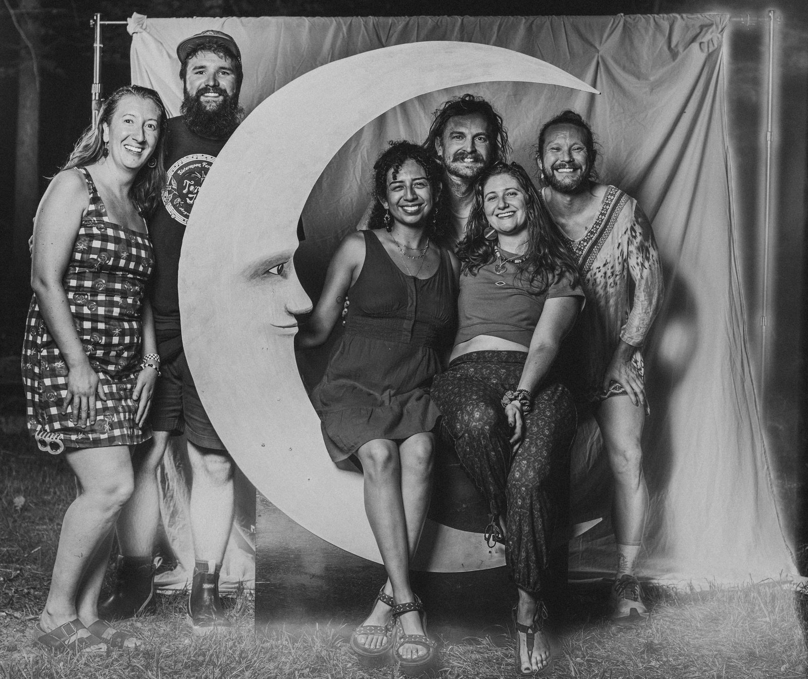 A whole crew crowded around the crescent moon at the Moon Booth, in black and white