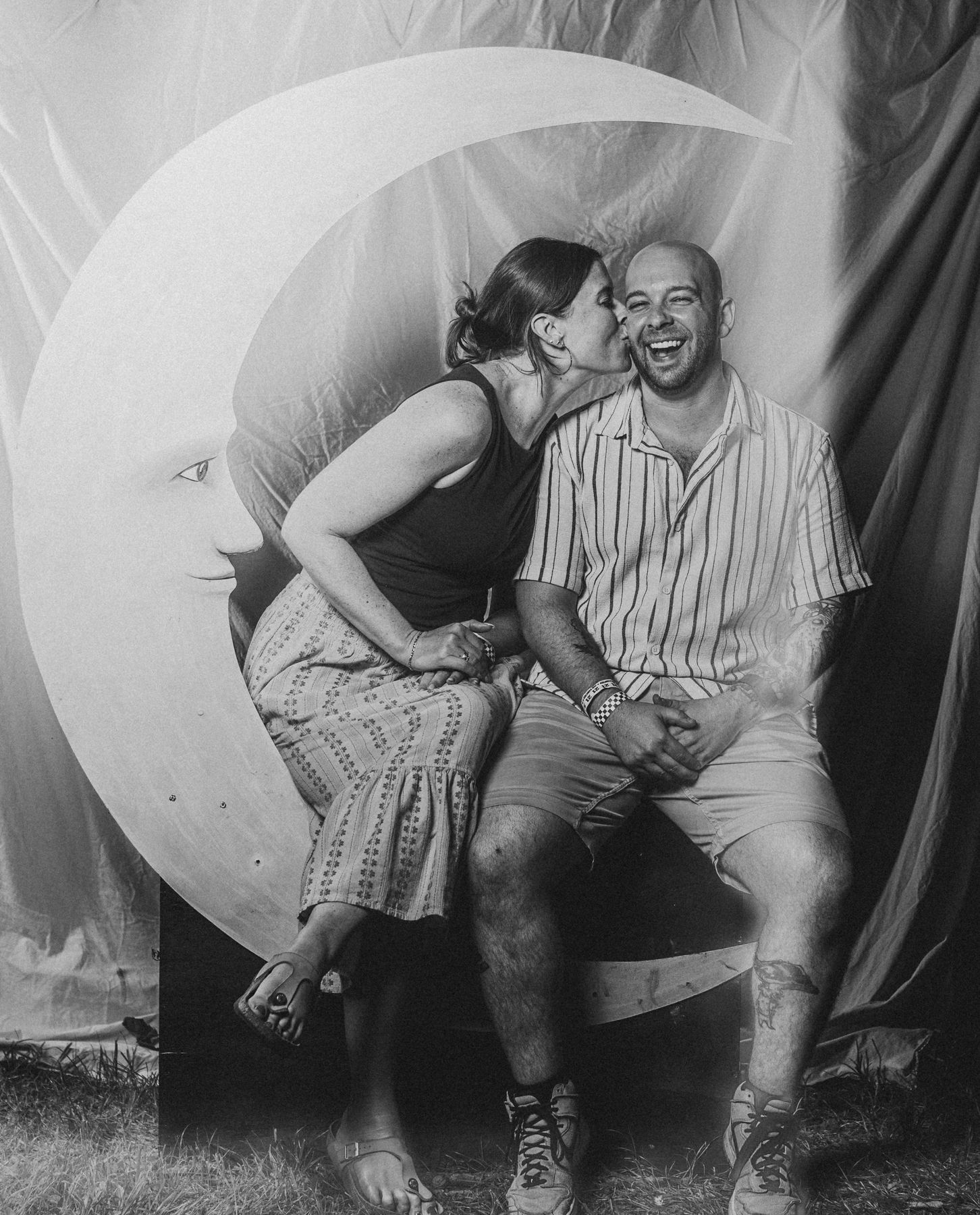 A woman kissing her laughing partner on the cheek at the Moon Booth, in black and white