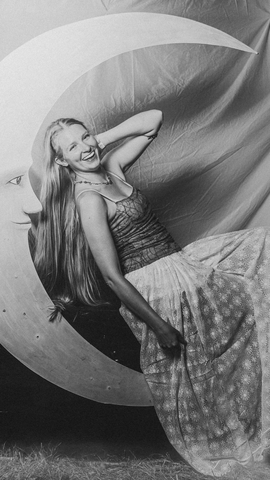 A woman in a long skirt reclining in the curve of the crescent moon, in black and white