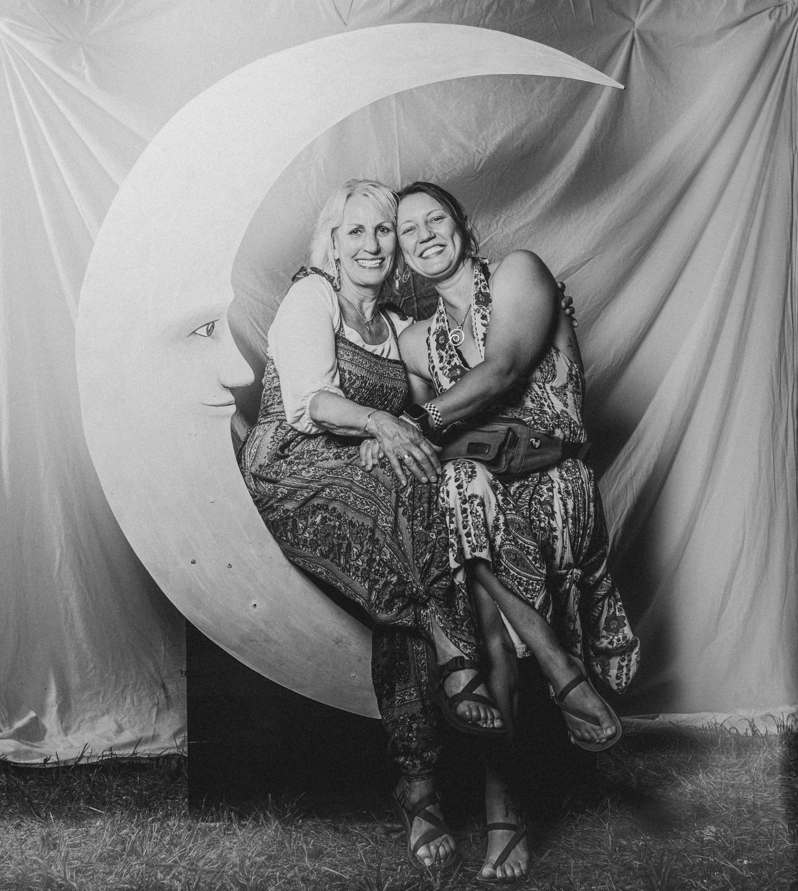 Two women laughing with their heads together on the crescent moon, in black and white