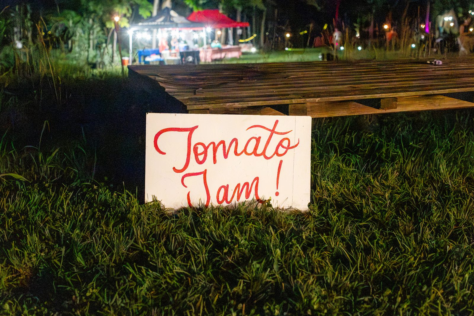 A hand-painted Tomato Jam sign leaning against wooden pallets in the grass at night