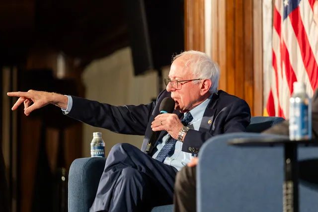 Bernie Sanders pointing into the audience while holding a microphone on the Press Club stage.