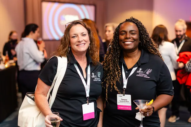 Two smiling attendees holding cocktails at an evening reception.