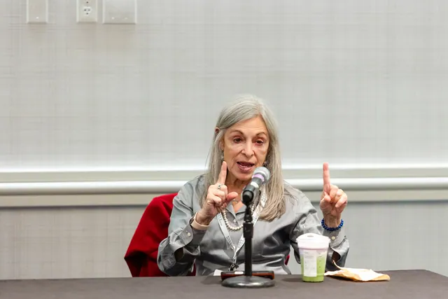 Panelist speaking animatedly with raised fingers at a table with a microphone.