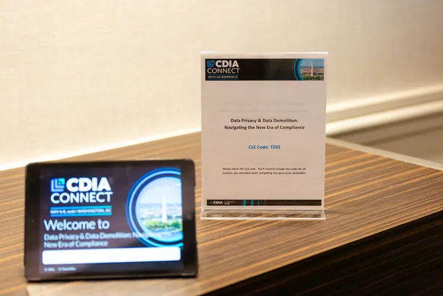Session welcome tablet and table sign showing the conference branding on a wood surface.