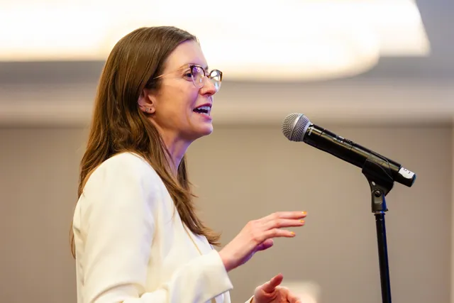 Attendee standing at a microphone asking a question with an engaged expression.