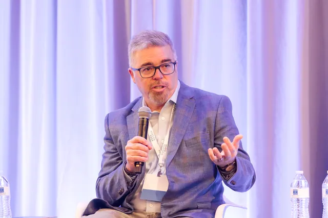 Panelist gesturing with open hand while speaking into a microphone.