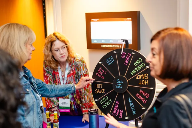Attendees gathered around a colorful prize wheel at a sponsor table.