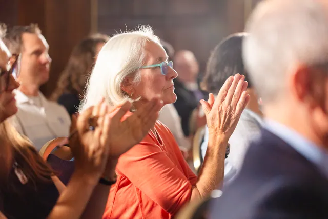 Audience member in a coral top applauding with warm, engaged expression during the panel.