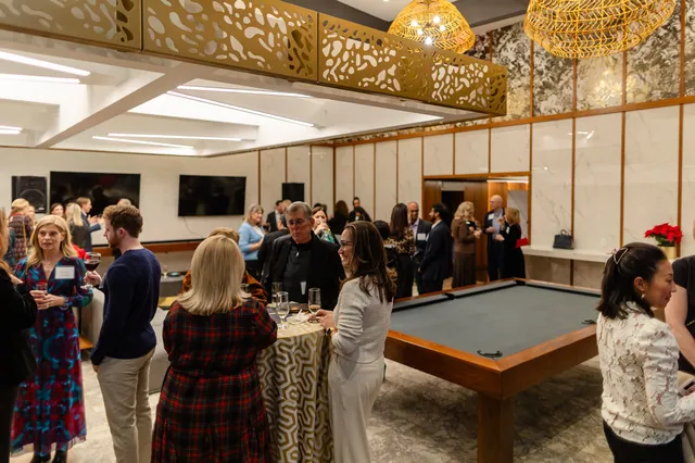A wide view of a gala reception with guests mingling around cocktail tables and a pool table under a gold ceiling.
