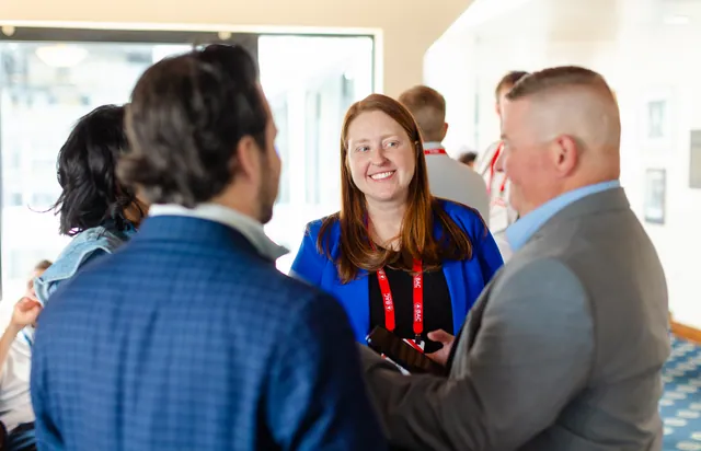Attendees in animated conversation in a bright room, one of them laughing.
