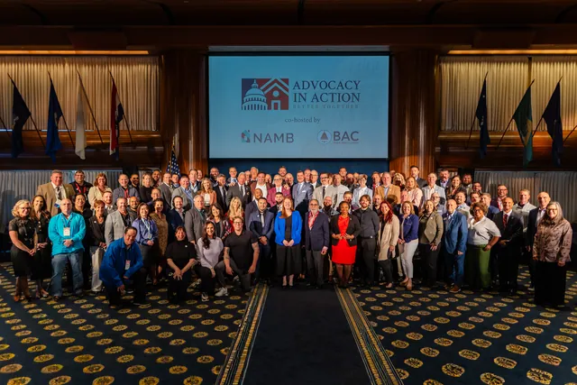 Large group photo of all attendees in a ballroom beneath the event screen.