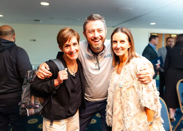 Three attendees with arms around each other laughing for the camera.