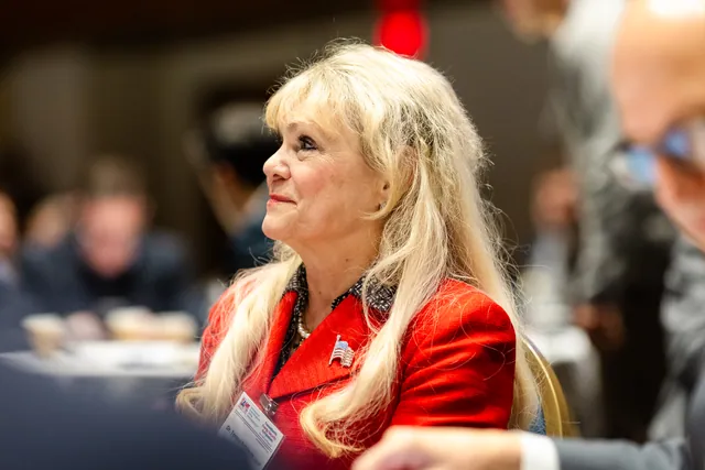 Attendee in a red jacket looks up attentively from the audience with soft background blur.